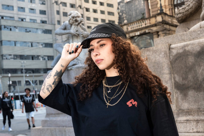 Young woman in a black outfit wearing a 4Msb 5-panel cap Kilian Zehnder tgraffiti in black with white texting