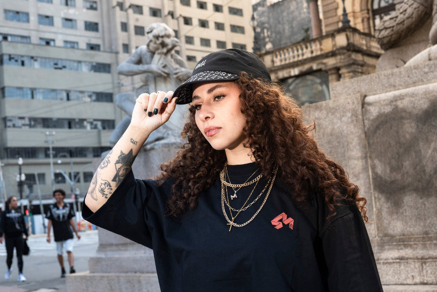 Young woman in a black outfit wearing a 4Msb 5-panel cap Kilian Zehnder tgraffiti in black with white texting