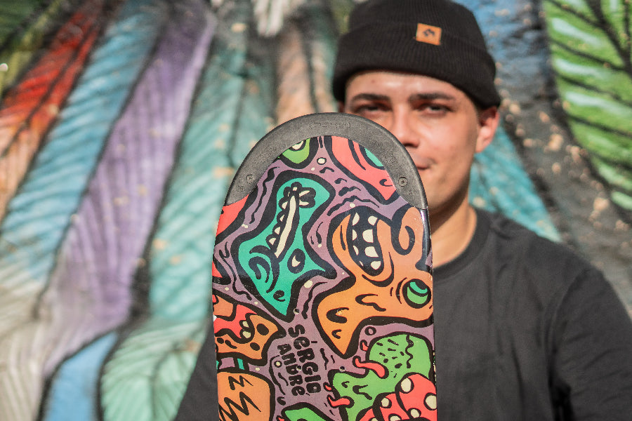 4Msb Pro rider Sérgio André with his signature skateboard deck Doodle Sérgio André, multicolour with TIPtech, infront of a colourful graffiti wall.