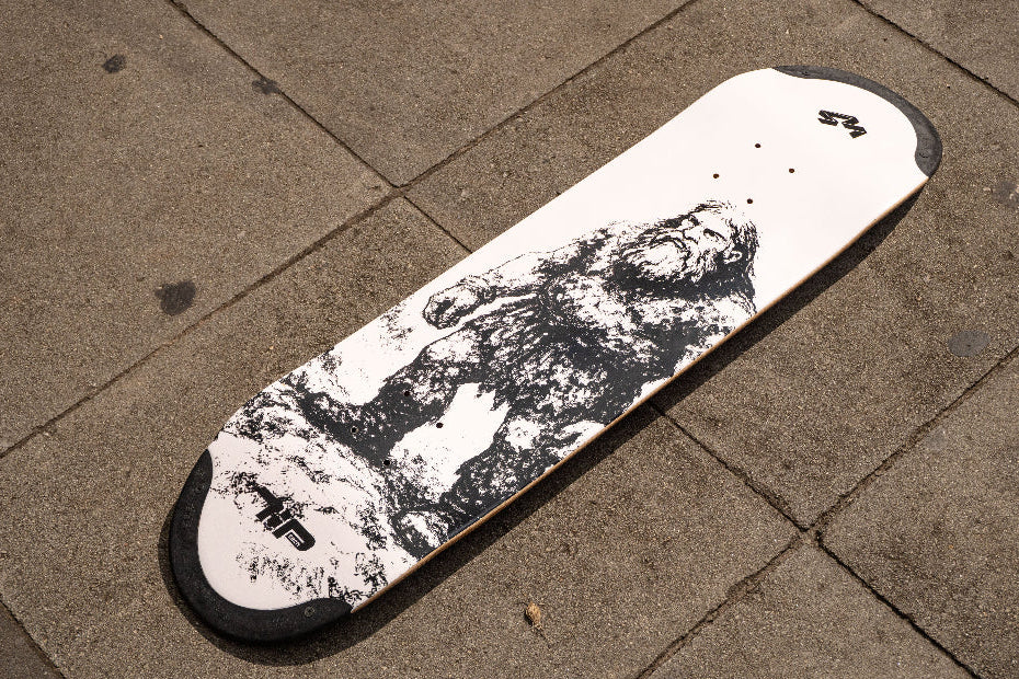 4Msb skateboard deck Jättar (Jattar) with TIPtech shown on the ground outdoor The graphic is black and white. A black giant (jätte/jättar in the swedish language) standing on stone ground against a white background.