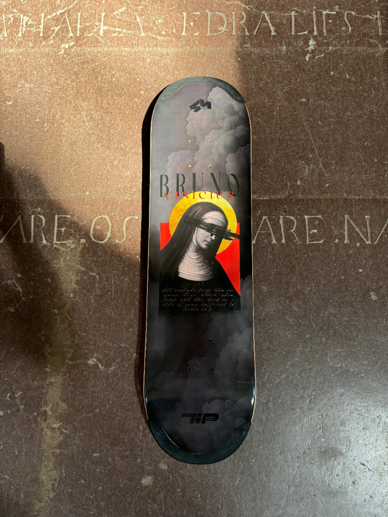 A 4Msb skateboard deck, part of the saints collection, photographed on the church floor. The graphic is dark grey and has an image of Saint Bridget with the title Bruno Vinicius.