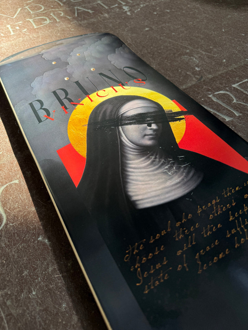 Close up of the 4Msb skateboard deck Saint Bridget, part of the saints collection, photographed on a church floor. The graphic is dark grey and has an image of Saint Bridget with a yellow halo and the title Bruno Vinicius, the 4Msb pro skateboarder.