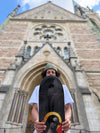 Pro Skateboarder Bruno Vinicius holding his 4Msb pro model skateboard deck Saint bridget, part of the saints collection, photographed outside the Oscar church in Stockholm, Sweden. The graphic is dark grey and has an image of Saint Bridget with a yellow halo and with the title Bruno Vinicius.