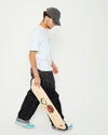 A skateboarder walking and holding a 4Msb skateboard deck Water Lily with TIPtech. He is wearing a grey 4Msb skateboard cap dala horse, an ice blue 4Msb t-shirt dala horse, dark jeans and light blue and white sneakers.