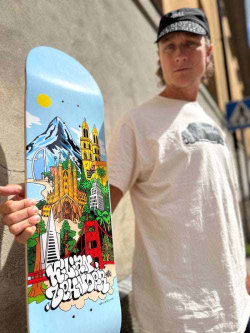 4Msb pro skateboarder Kilian Zehnder in white t-shirt holding his skateboard deck cities, pro model Kilian Zehnder. Colorful graphic of a cityscape with landmarks, trees and mountains on light blue background, showing Kilian Zehnder's four favorite cities: Barcelona, Sao Paulo, Zürich, San Francisco.
