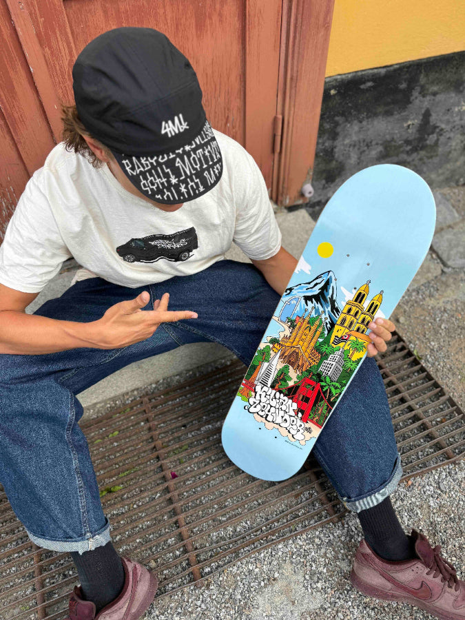 Pro skater Kilian Zehnder, wearing his skateboard cap graffiti, showing his new pro model, skateboard deck 'cities' classic shape (without TIPtech). The graphic of the deck has a light blue background, small yellow sun and skylines, mountains, towers, palm threes illustrating Kilian's four favorit cities.