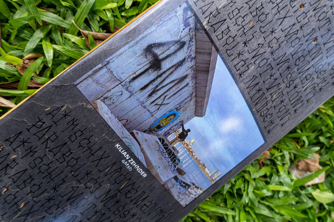 4Msb pro skater Kilian Zehnder's first pro model, signature deck, graffiti, seen laying in green grass. grey and blue graphic showing the rider kilian doing graffiti on a concrete wall by the sea in barcelona and personal text on the board including the words mission, mindset, movement, motivation, parabolic and aitsch