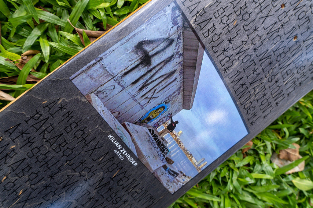 4Msb pro skater Kilian Zehnder's first pro model, signature deck, graffiti, seen laying in green grass. grey and blue graphic showing the rider kilian doing graffiti on a concrete wall by the sea in barcelona and personal text on the board including the words mission, mindset, movement, motivation, parabolic and aitsch