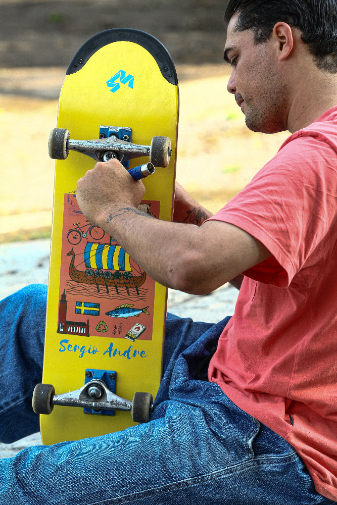 Pro rider Sérgio André holding his signature yellow Sverige TIPtech 4Msb skateboard deck with colorful design outdoors.