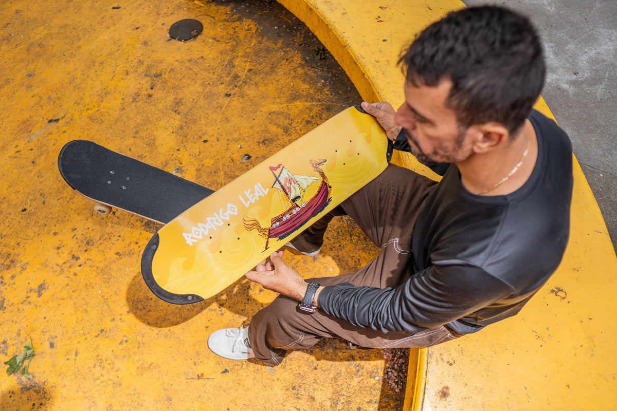 Pro skater Rodrigo Leal holding his pro TIP-tech deck, a yellow skateboard deck drakkar with a design of a ship.