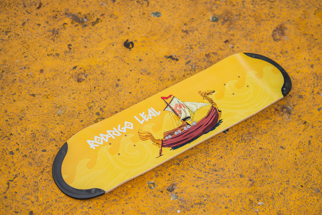 Pro skater Rodrigo Leal holding his pro TIP-tech deck, a yellow skateboard deck drakkar with a design of a ship.