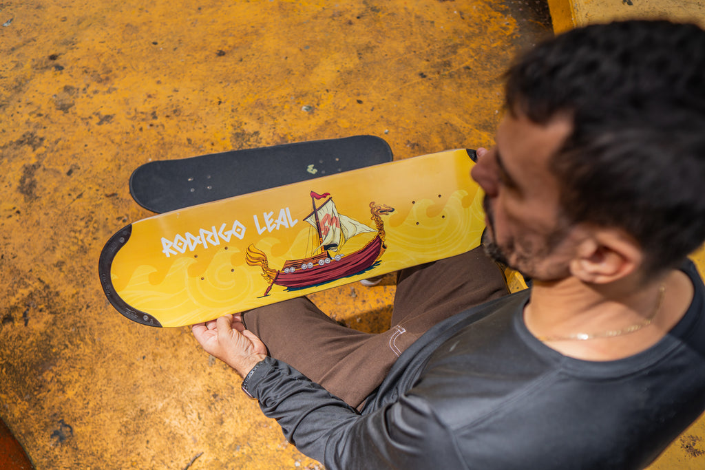 Pro skater Rodrigo Leal holding his pro TIP-tech deck, a yellow skateboard deck drakkar with a design of a ship.