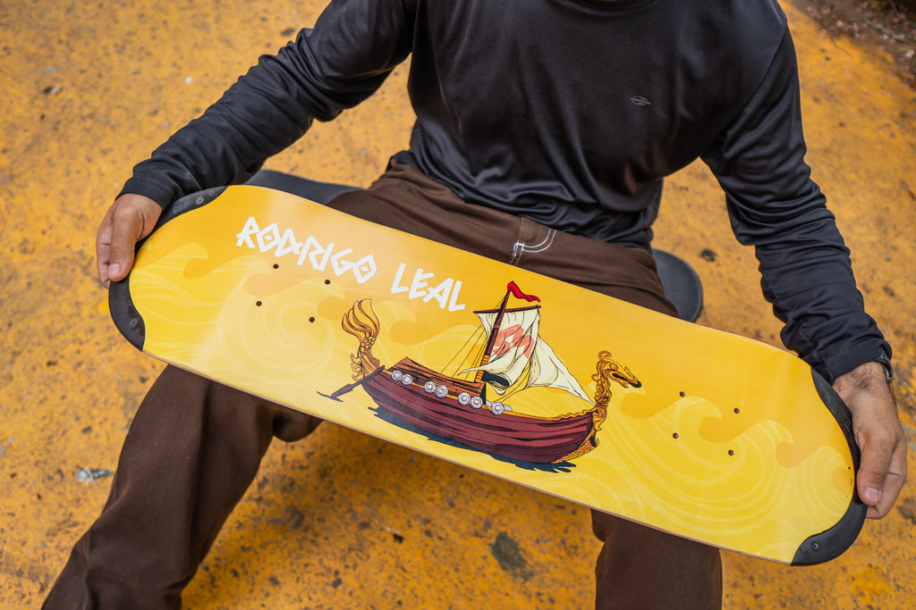Pro skater Rodrigo Leal holding his pro TIP-tech deck, a yellow skateboard deck drakkar with a design of a ship.