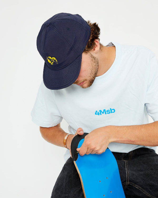 skateboarder wearing a navy blue snapback cap with a yellow dala horse on the front, a 4Msb t-shirt dala horse ice blue and adjusting a screw on the TIPtech skateboard deck.