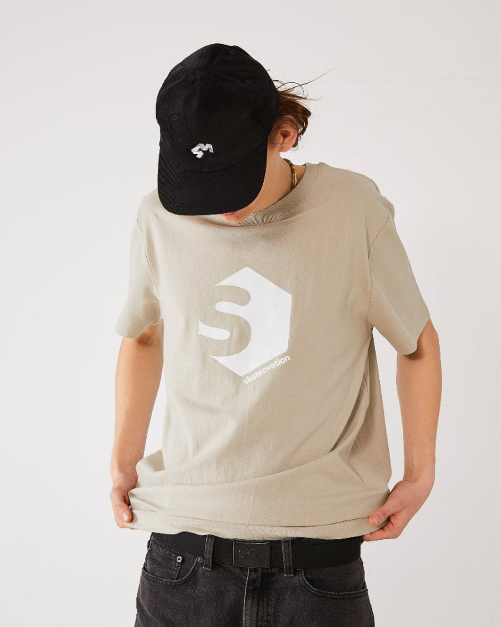 Skater wearing a beige skateovation t-shirt SO 720 colour stone, a black 4Msb corduroy cap and a black webbing belt SO with a black metal buckle.