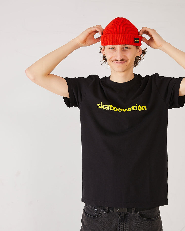 Skater wearing a black skateovation T-shirt Core and a skateovation fire red harbour beanie core.