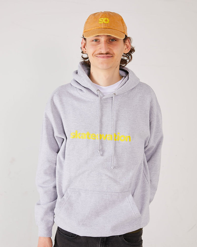 Skateboarder wearing a dad cap SO vintage mustard  and a skateovation hoodie core heather grey.