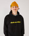 skater wearing a black hoodie with yellow 'skatevation' text and a mustard yellow harbour beanie.