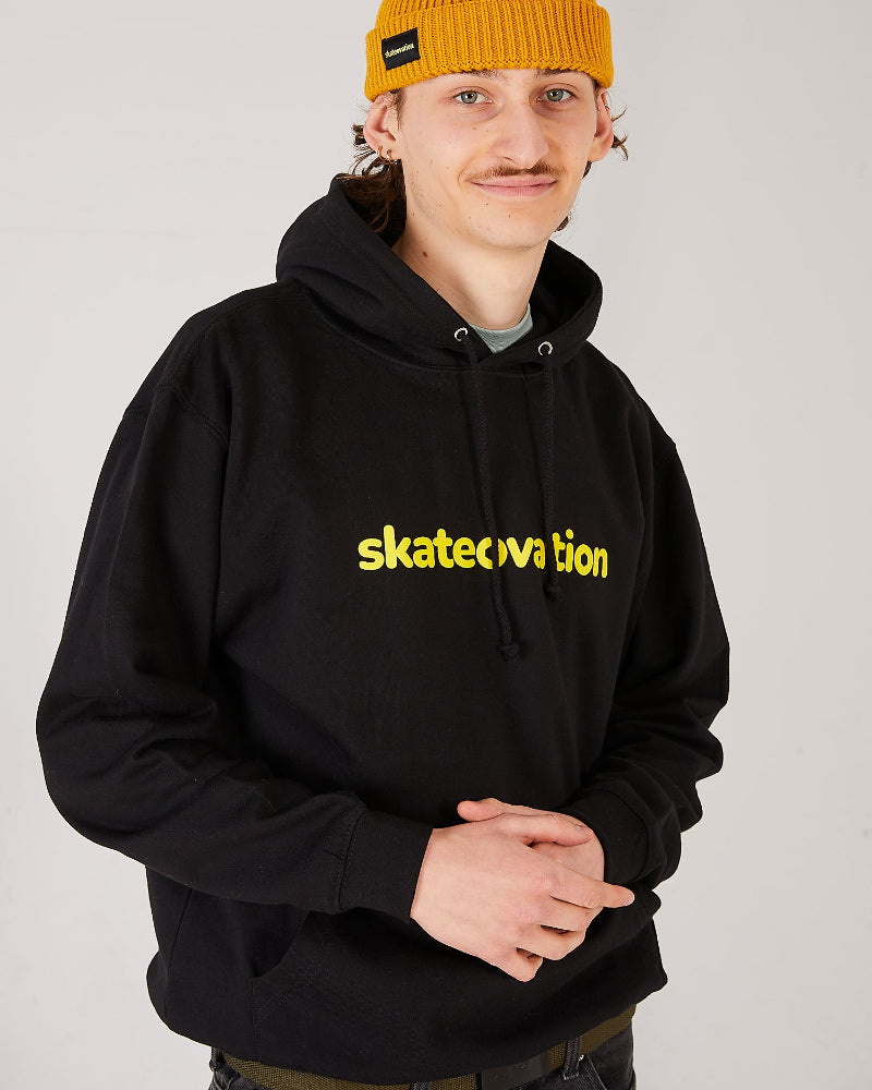 skater wearing a black hoodie with yellow 'skateovation' text and a mustard yellow harbour beanie.