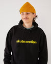 skater wearing a black hoodie with 'skatevation' text and a mustard coloured harbour beanie core.