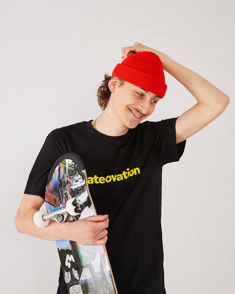 skater wearing a black t-shirt with skateovation text, holding a 4Msb skateboard, and adjusting a red harbour beanie