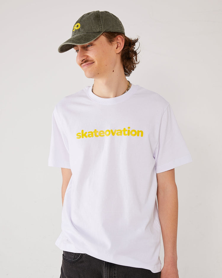 Skater facing forward, head in profile, wearing a Skateovation t-shirt core in white color with skateovation texted in yellow on the chest and a dad cap SO in the color vintage olive with SO embroidered in yellow on the front.