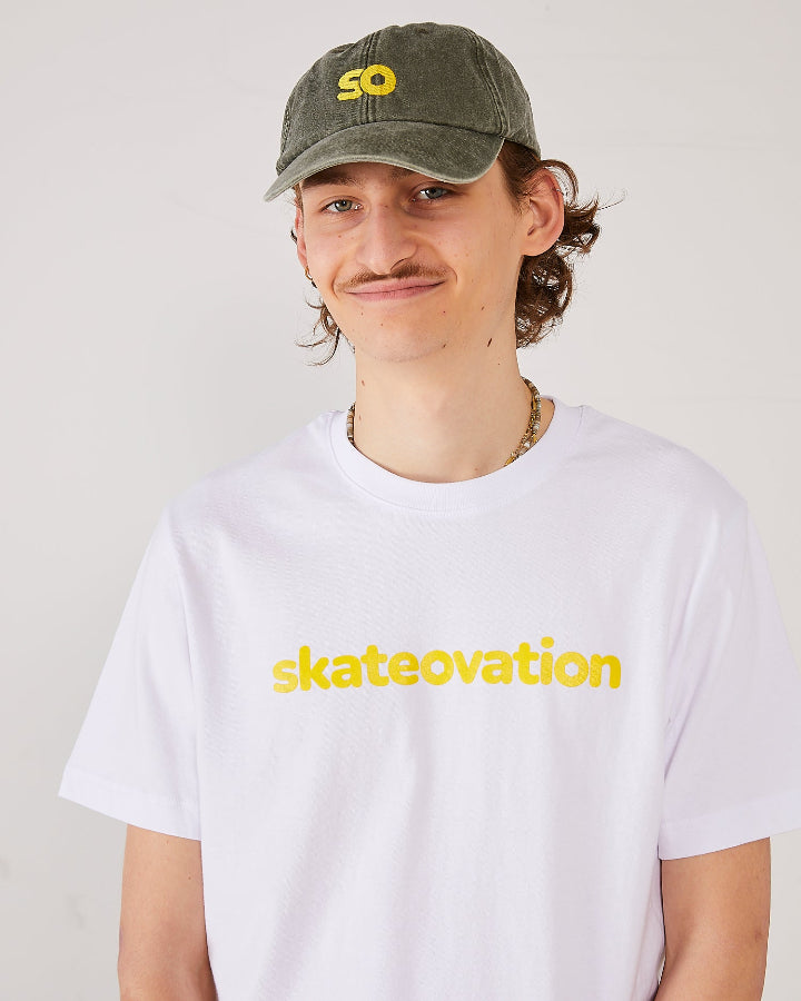 Skater facing forward wearing a white Skateovation t-shirt core with skateovation texted in yellow on the chest and a dad cap SO in the color vintage olive with SO embroidered in yellow on the front.