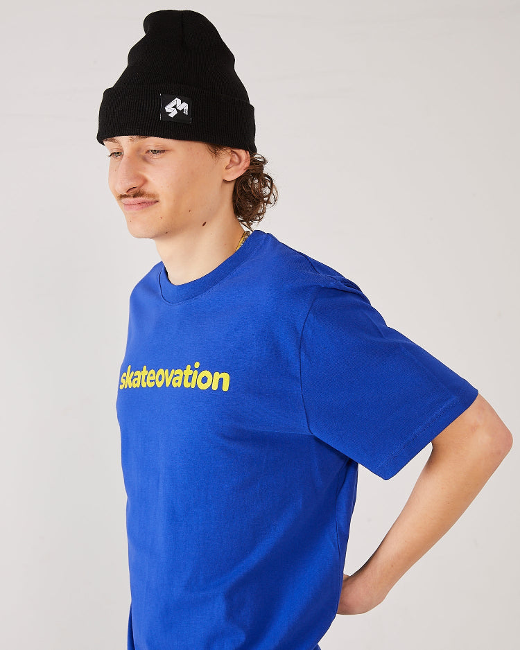 Skater wearing a Skateovation t-shirt Core in color worker blue, skateovation texted in yellow on the chest and a 4Msb cuffed beanie Quatro in black.