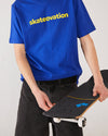 Skater wearing Skateovation t-shirt Core colour worker blue with skateovation texted in yellow on the chest, holding a TIPtech skateboard deck with 4Msb griptape Quatro and wheels Quatro in black and white.