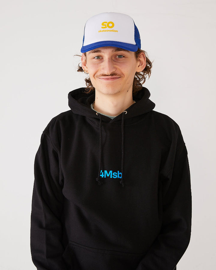 Skateboarder wearing a black 4Msb hoodie and a blue and white skateovation SO trucker cap.