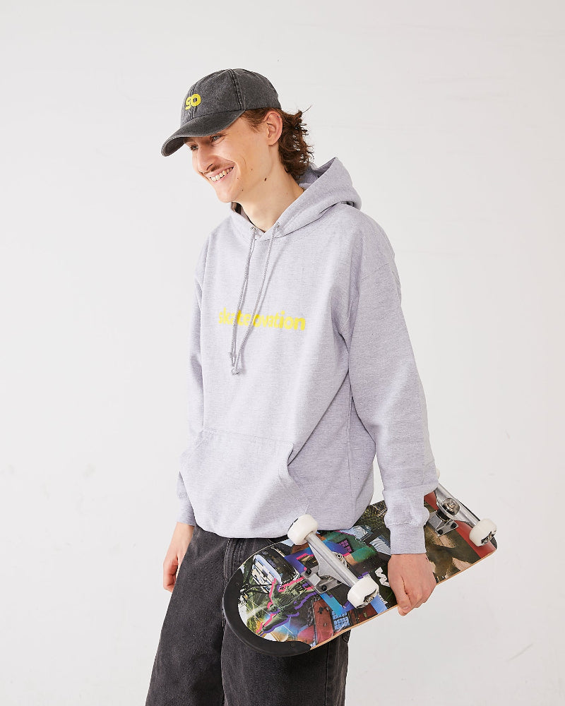 Skater wearing a grey skateovation hoodie with yellow text and a SO dad cap, holding a colorful 4Msb skateboard Collage Englebrek.