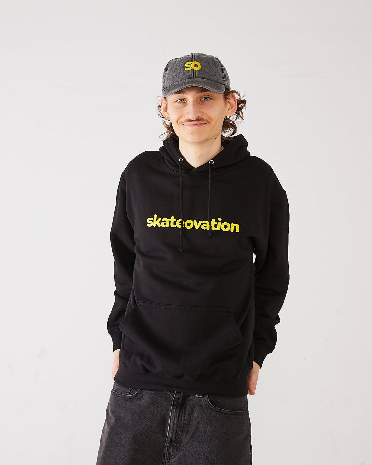 Skater wearing a dad cap in vintage black with SO logo in yellow and a black hoodie core with Skateovation texted in yellow.