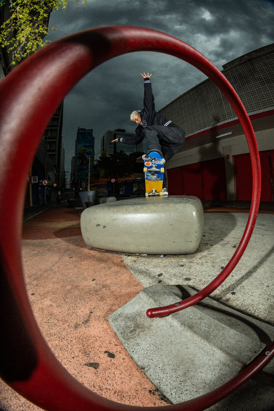 Skateboarder Joao Richter performing a trick on a concrete ledge with a red metal hoop in the foreground. 4Msb skateboard deck Fisher with TIPtech