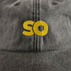 Vintage black dad cap close-up of embroidered 'SO' logo in yellow on the front.